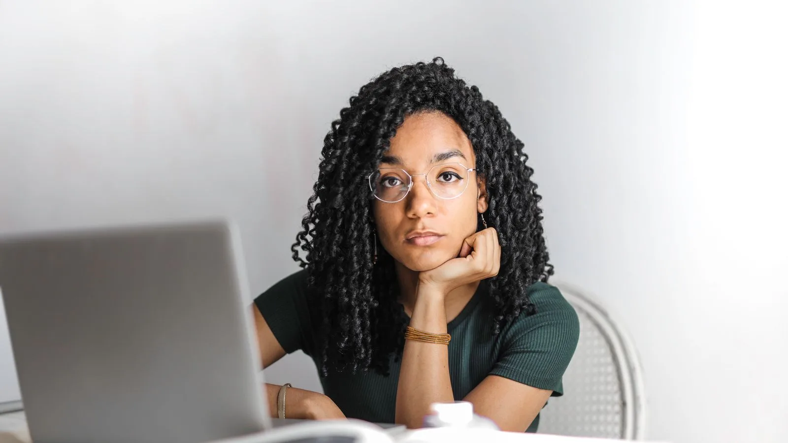 A woman at a laptop looking up from the screen with a sceptical expression.
