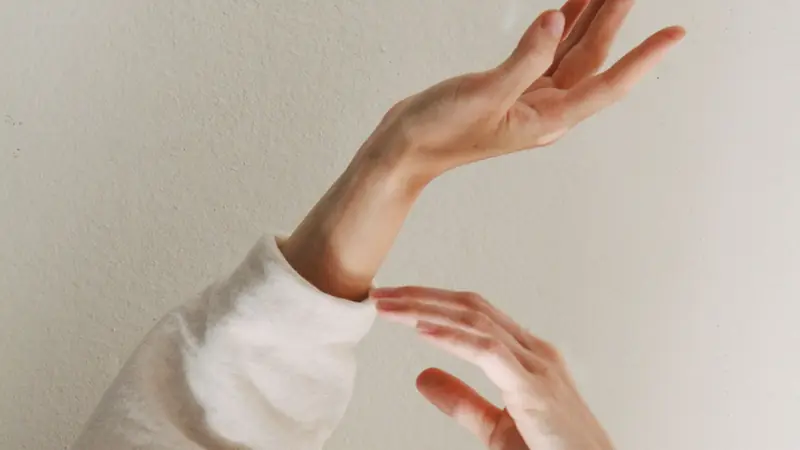 A person in a cream sweater raising both hands against a warm neutral wall.