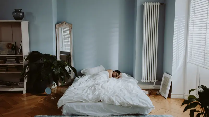 A person asleep under a white duvet in a calm, softly lit bedroom.
