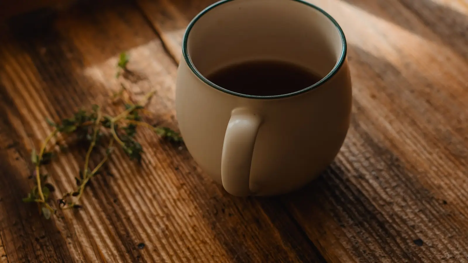 A ceramic mug of coffee on a worn wooden table beside a sunlit window.