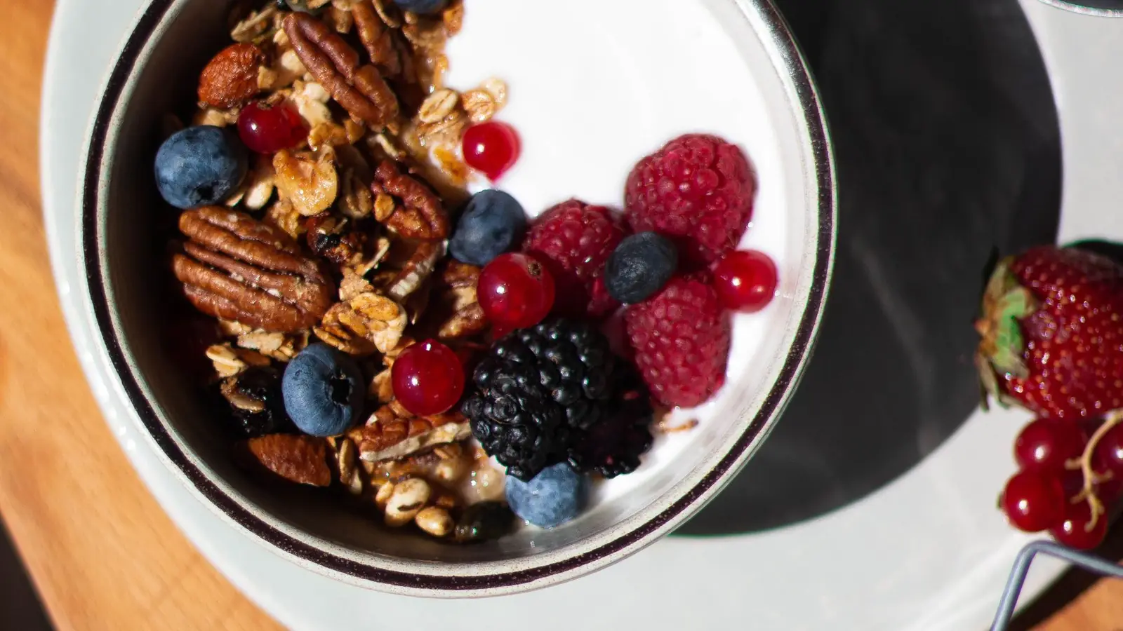 An overhead view of a breakfast bowl of granola, yoghurt and berries on a wooden table.