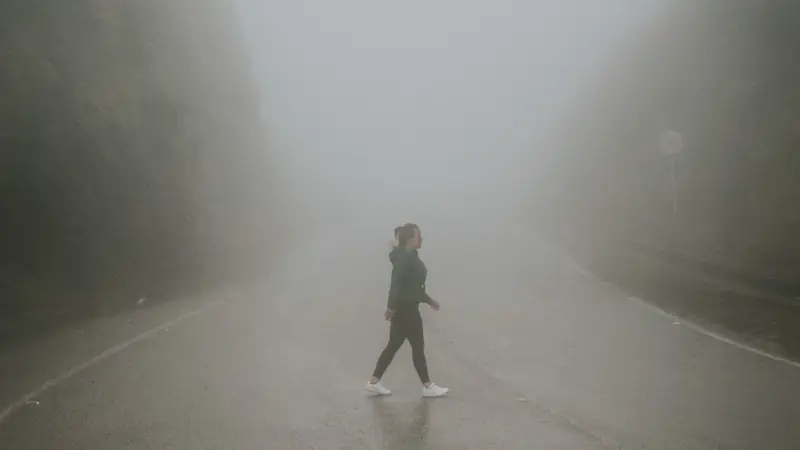 A person walking across an empty road in heavy morning mist.