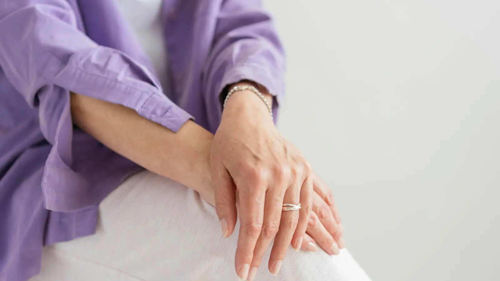 A person’s hands resting on their knee, wrists bare, in soft daylight.
