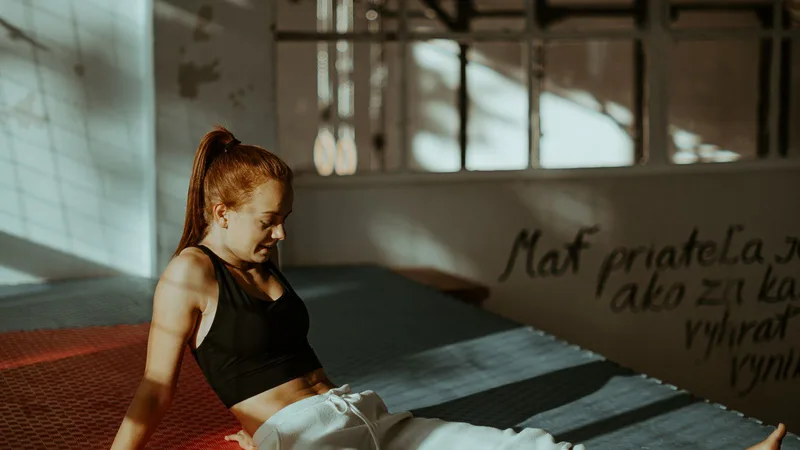 An athlete sitting on a gym mat in low afternoon light, looking down and thinking.